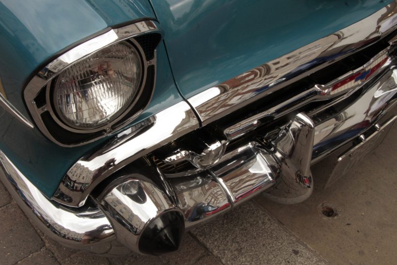 Classic 1957 Chevrolet Bel Air, featuring a teal-painted body, round headlight with a hooded chrome bezel, & stylish chrome bumper assembly