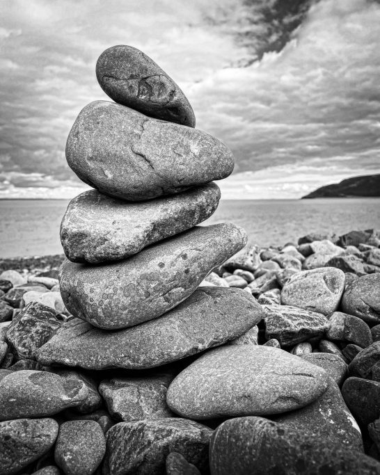 Black and white image of a small tower of stones piled up on a beach in Wales