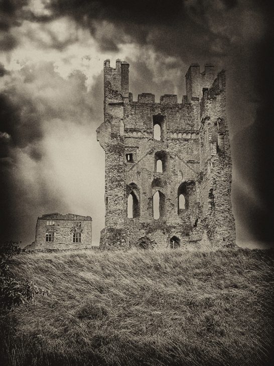 Haunting image of a castle ruin isolated on a hillside with stormy clouds in the background