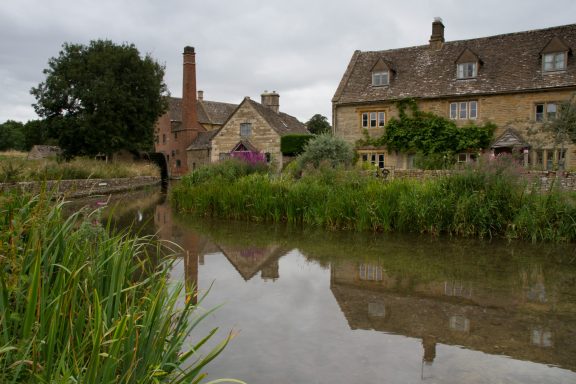 The image shows The Old Mill and traditional cottages along the River Eye in Lower Slaughter, Gloucestershire