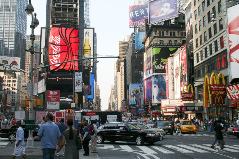 A busy street scene in Times Square, New York City, featuring large billboards and bustling traffic.
