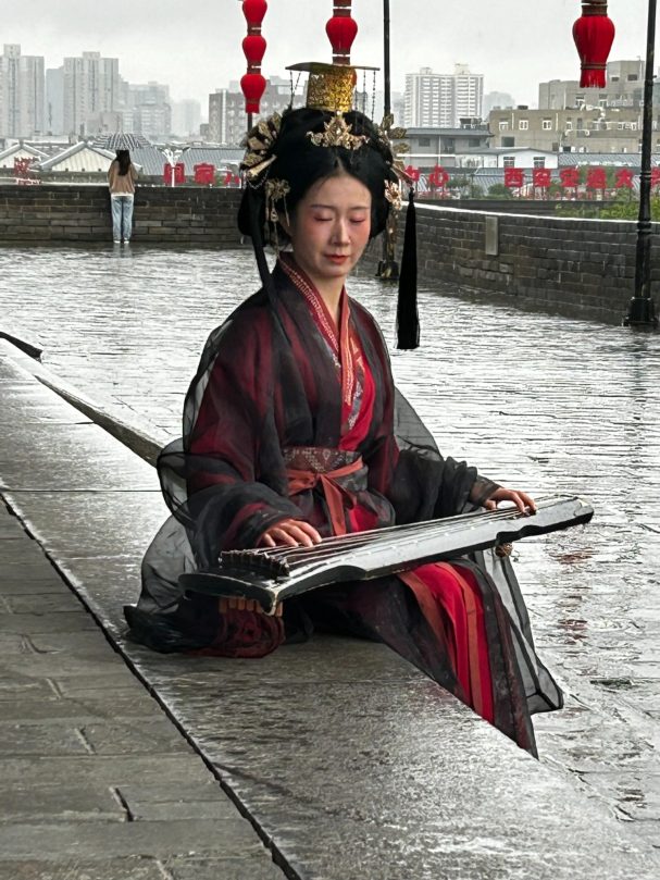 Chinese woman dressed in customary costume and playing Guzheng stringed instrument