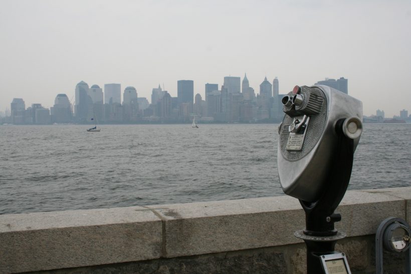 Coin-operated binoculars overlooking New York skyline from a pier, capturing iconic skyscrapers.